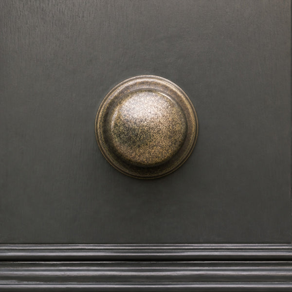  A round, antique bronze doorknob with a textured, speckled finish mounted on a dark charcoal-colored wooden door.