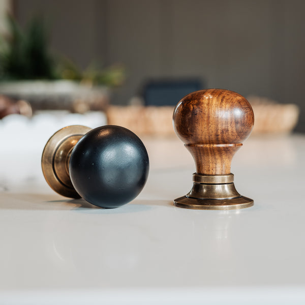  Two wooden door knobs, one black and one brown, on a white surface with a blurred background.