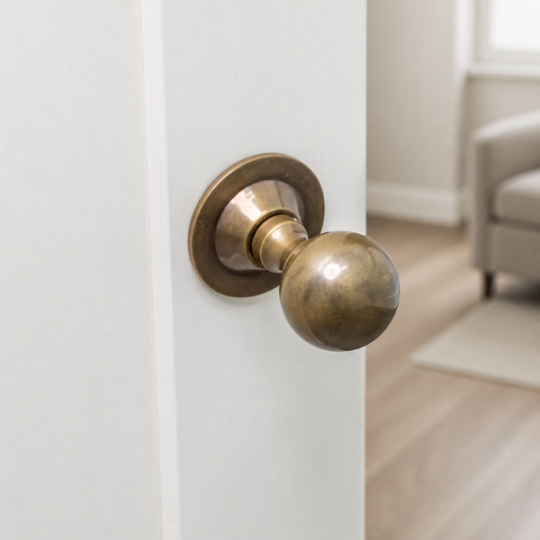 A close-up of a round brass door knob mounted on a white door, with a softly blurred living room interior in the background.