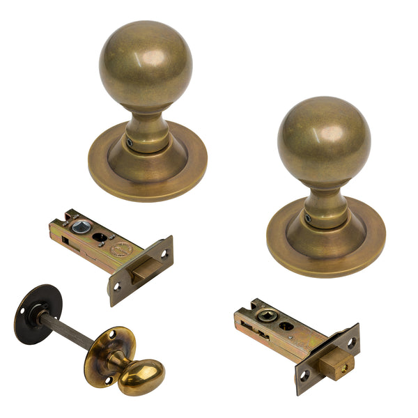   A set of brass door hardware components on a white background, including two round doorknobs with round bases, two latch bolts with backplates, and a thumbturn knob with a backplate.