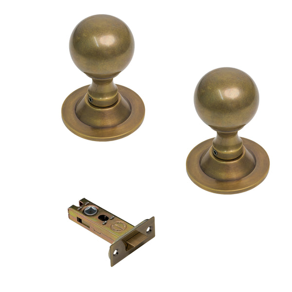   Two brass ball door knobs with round ball handles and round backplates, shown alongside a matching metal latch strike assembly on a plain white background.