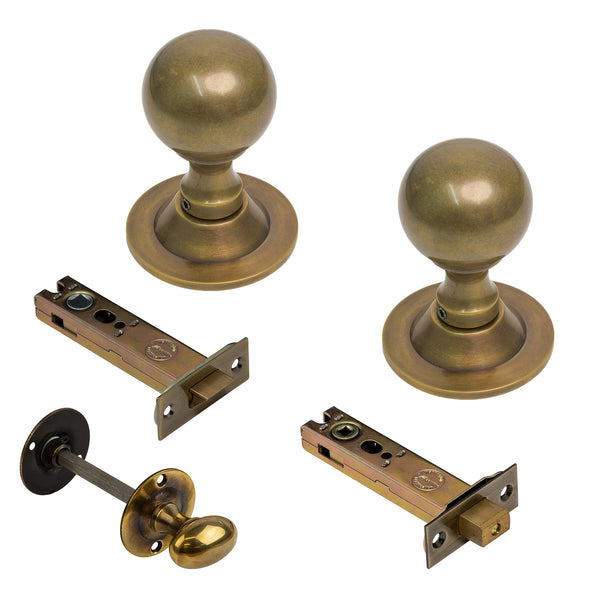  A set of antique brass door hardware including two round doorknobs with round bases, two latch bolts with backplates, and a round thumbturn knob, all shown on a plain white background.