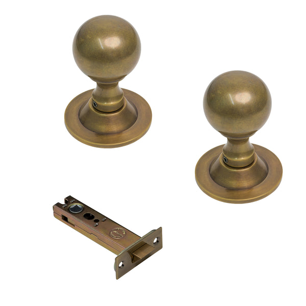  Two round brass door knobs with round bases and a matching metal latch plate, shown on a plain white background.